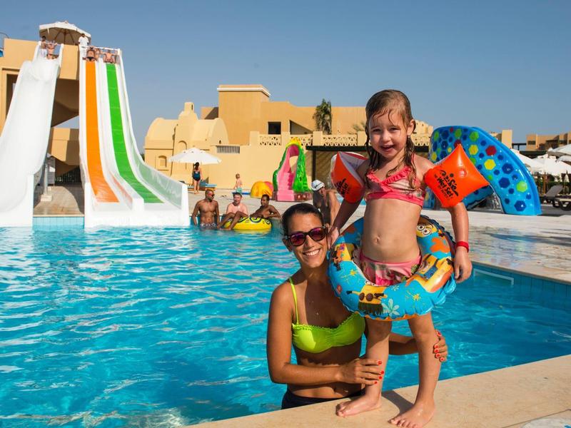 Donna e bambina in piscina con scivoli acquatici sullo sfondo.