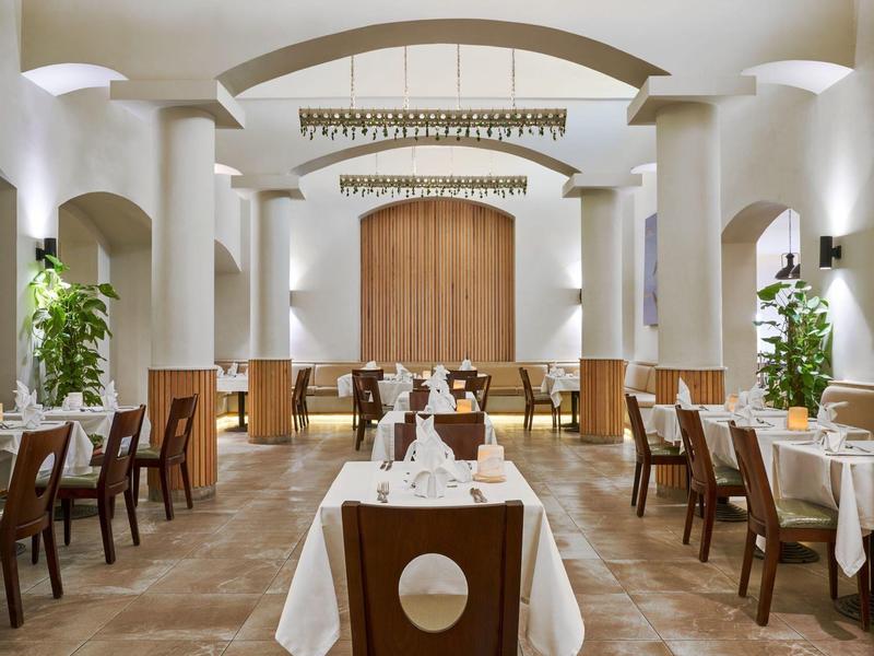 Sala da pranzo elegante con tavoli bianchi, sedie in legno e colonne bianche.