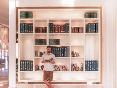 Uomo appoggiato a una libreria piena di libri in uno spazio luminoso.