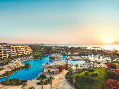 Weitläufiges Resort mit Pools, Garten und Meerblick bei Sonnenuntergang.