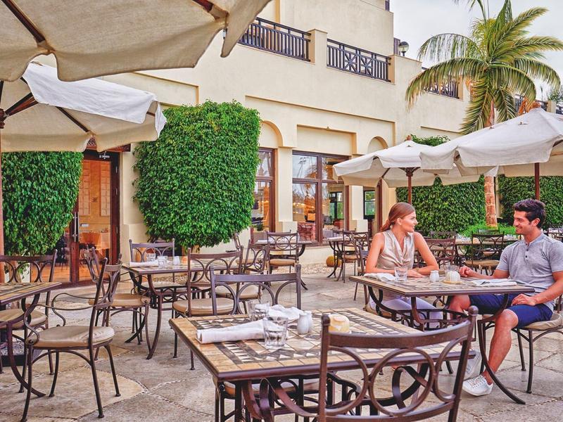 Buitenrestaurant met tafels en stoelen, twee gasten zitten onder parasols.