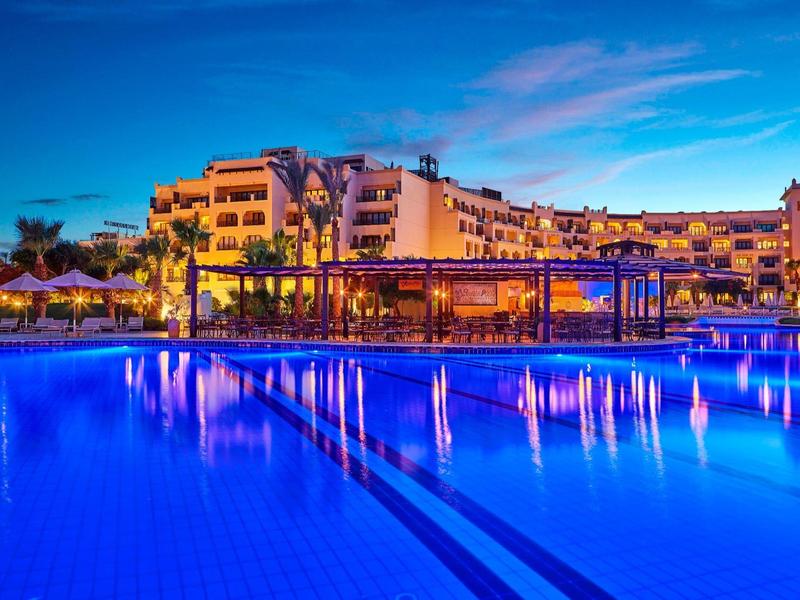 Verlicht hotelzwembad 's nachts met palmbomen en heldere blauwe lucht.