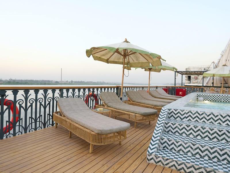Terrasse sur le toit avec chaises longues, parasol et vue sur la mer sous un ciel clair.