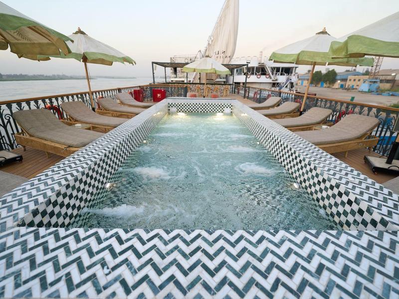 Bain à remous moderne avec motif noir et blanc, entouré de chaises longues et parasols au bord de l'eau