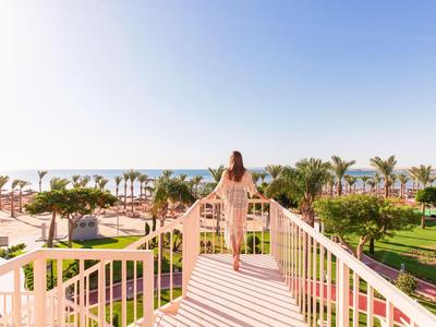 Femme sur balcon avec vue sur palmiers, jardin et mer sous un ciel clair