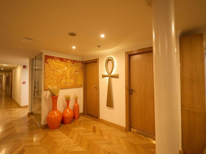 Verlichte hotelgang met houten vloer, decoratieve vazen en wandkunst.