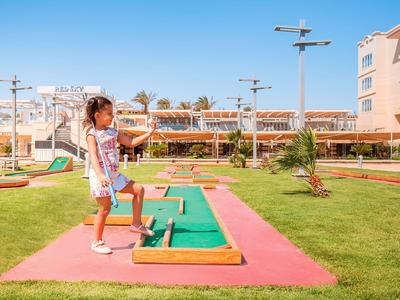 Dvě děti hrají minigolf na barevném hřišti vedle hotelu za slunečného počasí.