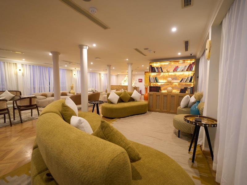 Przytulna strefa wypoczynkowa hotelu z zielonymi sofami, fotelami i ciepłym oświetleniem.