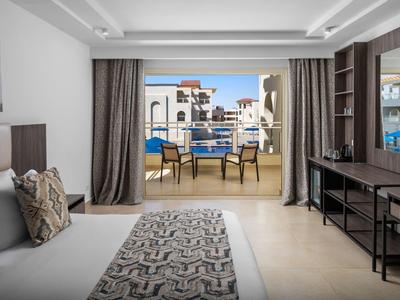 Chambre d'hôtel moderne avec lit, bureau, balcon avec chaises et vue sur les bâtiments.