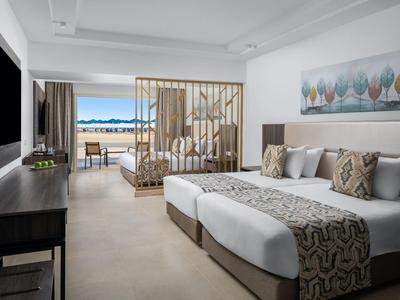 Chambre d'hôtel moderne avec lit double, coin salon et balcon avec vue sur la mer.