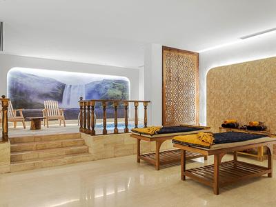 Espace spa lumineux avec deux tables de massage, jacuzzi privé et cloison décorative en bois.