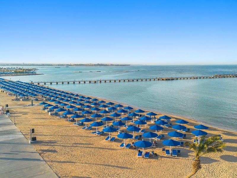 Plage avec parasols bleus et promenade au bord de la mer sous un ciel clair.
