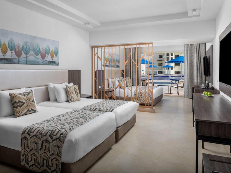 Chambre d'hôtel moderne avec deux lits, coin salon et grand téléviseur.