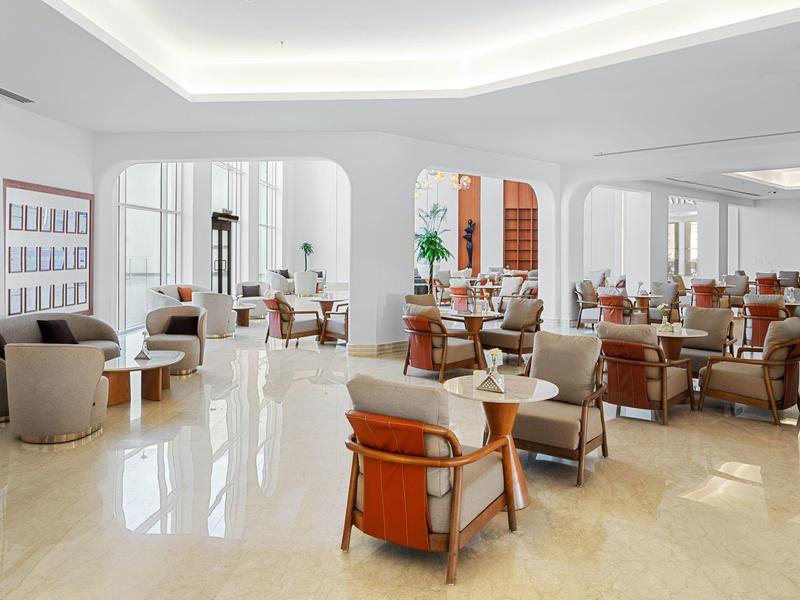 Espace lounge d'hôtel lumineux et moderne avec des fauteuils confortables et un sol réfléchissant.