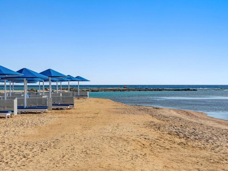 Plage de sable vide avec parasols bleus et mer calme par une journée ensoleillée