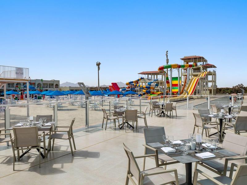 Terrasse vide avec tables et chaises devant un parc aquatique avec toboggans sous un ciel dégagé