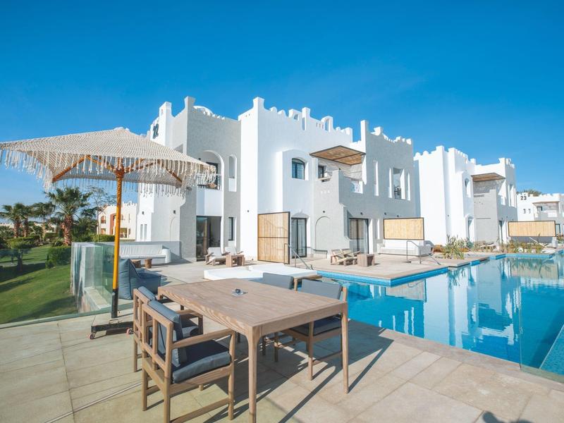 Hotel bianco moderno con piscina esterna e tavolo con sedie sotto ombrellone.