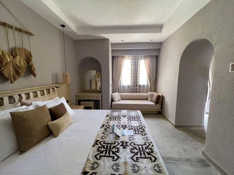 Camera d'albergo luminosa con letto grande, cuscini marroni e divano vicino alla finestra.