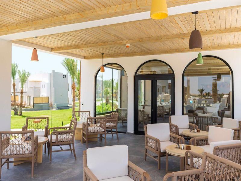 Terrazza esterna con poltrone in rattan sotto un tetto di legno, vista su giardino e hotel.