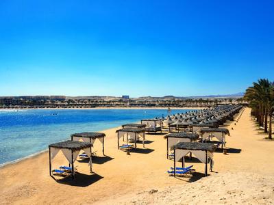 Plage ensoleillée avec cabanes, chaises longues et eau bleue calme.