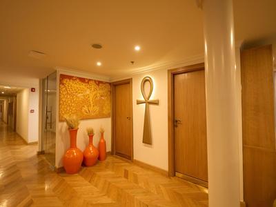 Pasillo de hotel bien iluminado con suelo de madera, varias puertas y jarrones decorativos.