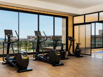 Modern fitness equipment in a bright room with large windows overlooking the pool.