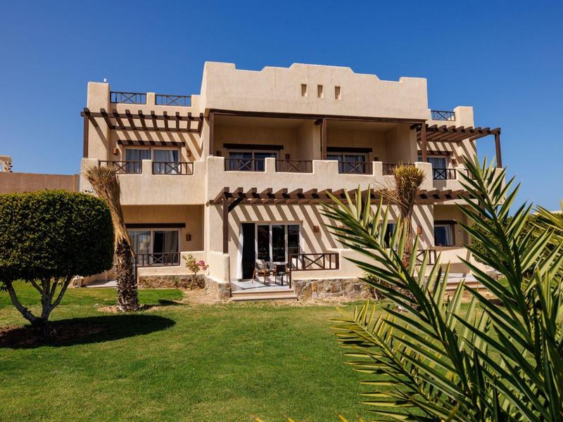 Zweistöckiges beige Gebäude mit Balkonen, grünem Rasen und klar blauem Himmel im Hintergrund.