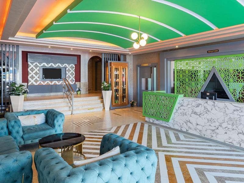 Salone dell'hotel con divani blu, banco in marmo bianco e soffitto verde curvo.