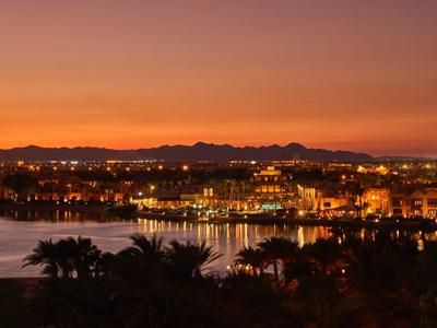 Tramonto su una città costiera illuminata con palme in primo piano.