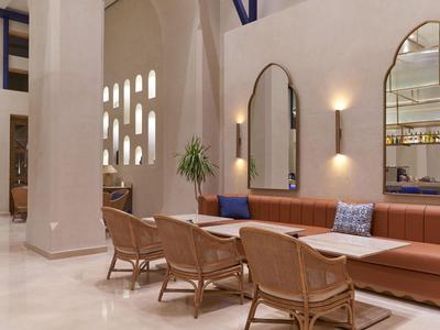 Interno di un salone d'hotel elegante con divani in pelle, sedie in vimini e grandi specchi.