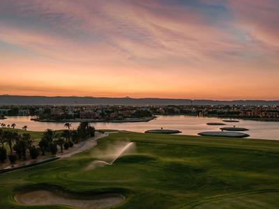 Un campo da golf verde con un lago al tramonto dai colori caldi.