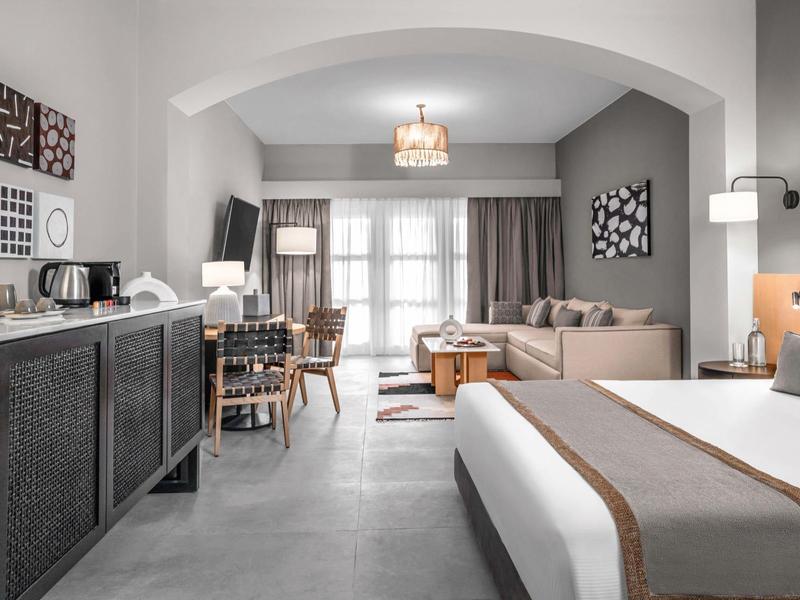 Camera d'hotel moderna con letto matrimoniale, divano, scrivania e decorazioni semplici.