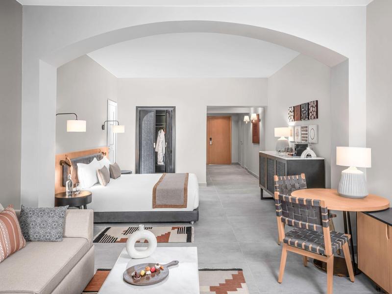 Ampia camera d'hotel con letto matrimoniale, divano e scrivania moderna, arredamento neutro.