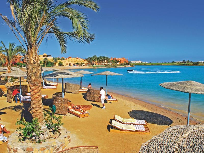 Spiaggia soleggiata con palme, lettini e ombrelloni vicino ad acqua azzurra e limpida.