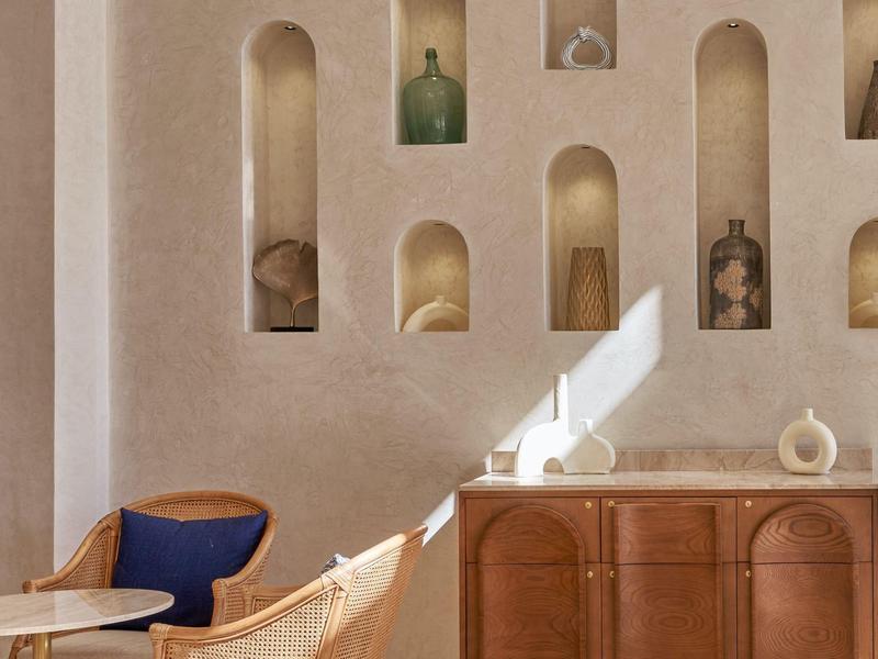 Interno minimalista con muro beige, nicchie decorative e poltrona blu in un soggiorno accogliente.