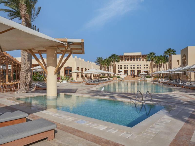 Piscina esterna con lettini e ombrelloni in un resort sotto un cielo azzurro.