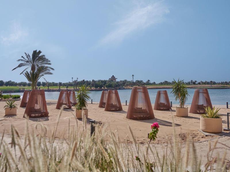 Lettini con tende su una spiaggia sabbiosa vicino a un lago sotto un cielo azzurro.