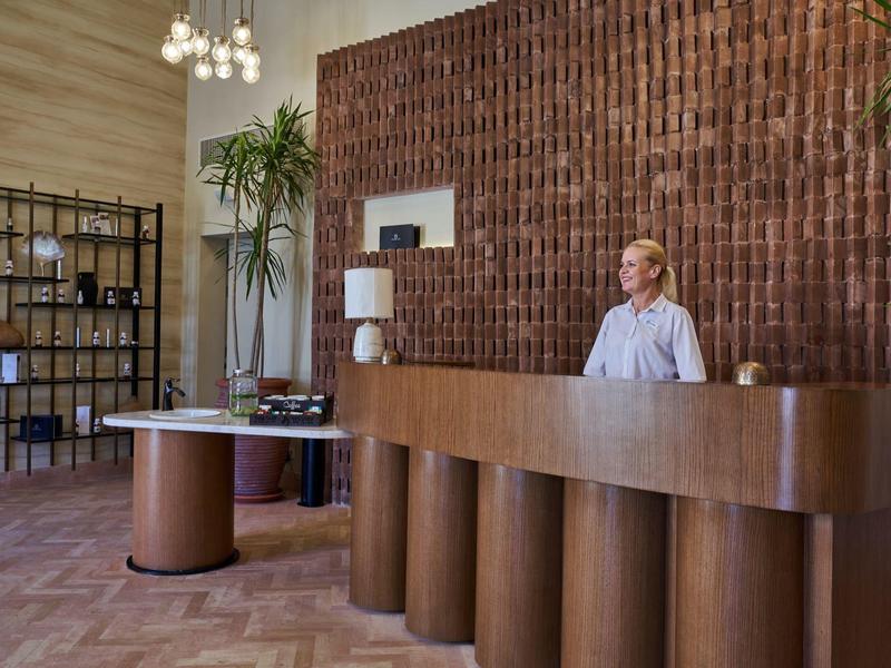 Reception di hotel moderna in legno con banco curvo e una dipendente in piedi.