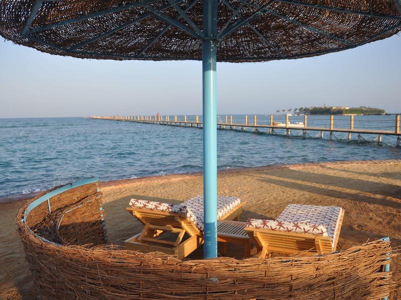 Area relax con sedie a sdraio e ombrellone vicino all'acqua e a un pontile.