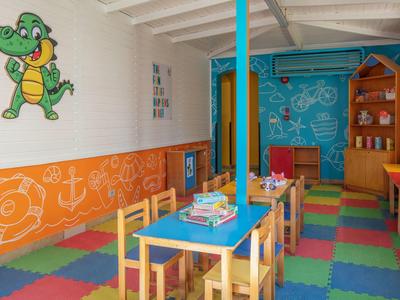 Sala giochi colorata con tavoli, sedie e decorazioni murali divertenti.