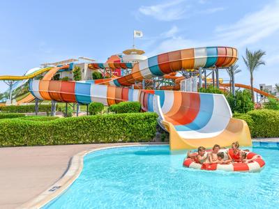 Bambini scendono uno scivolo d'acqua colorato in una piscina sotto un cielo azzurro.