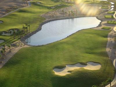 Campo da golf con lago, bunker e erba verde al tramonto.