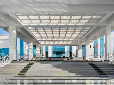 Entrée moderne avec grand escalier et auvent en verre dans un bâtiment hôtelier.