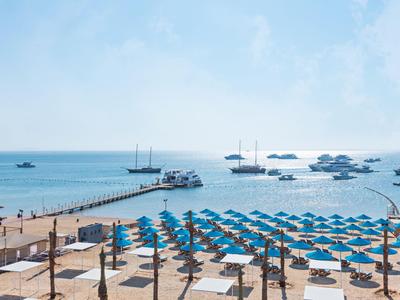 Plage avec parasols bleus, chaises longues et une jetée s'étendant dans une mer bleue calme sous un ciel clair
