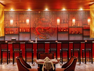 Bar d'hôtel élégante avec bois sombre, accents rouges et fauteuils confortables au premier plan.