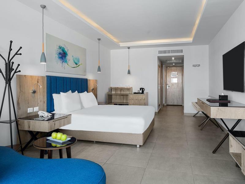 Camera d'hotel moderna con letto matrimoniale, poltrona blu e decorazione minimalista.