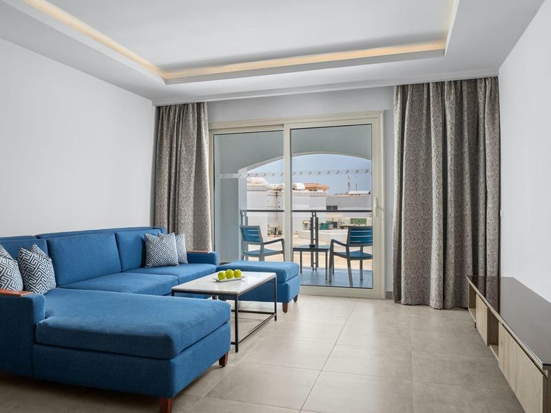 Soggiorno moderno con divano blu, tavolino e balcone soleggiato.