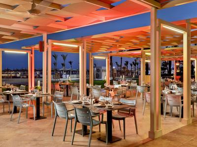 Restaurante al aire libre con mesas preparadas y vista de palmeras iluminadas al anochecer.
