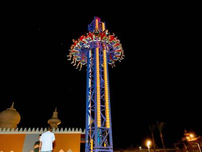 Torre de atracción de caída libre colorida de noche con personas y edificio iluminado al fondo