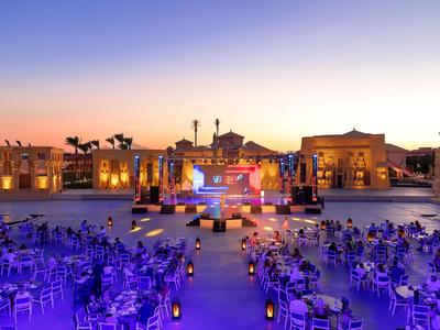 Lounge abierta con asientos y escenario al atardecer en un resort hotelero.